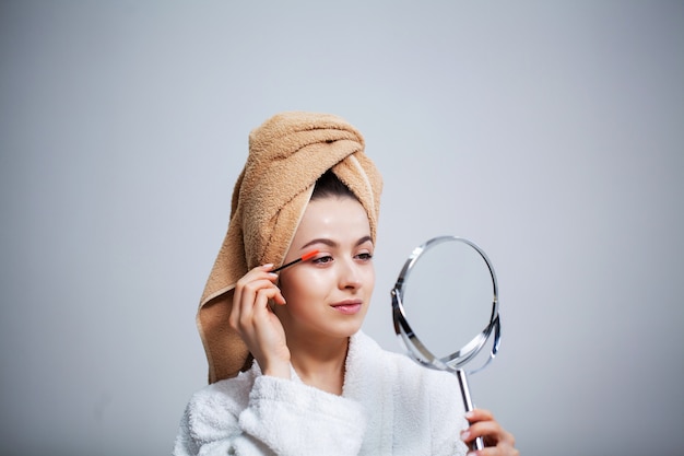 Pretty young woman puts makeup on the face in the bathroom