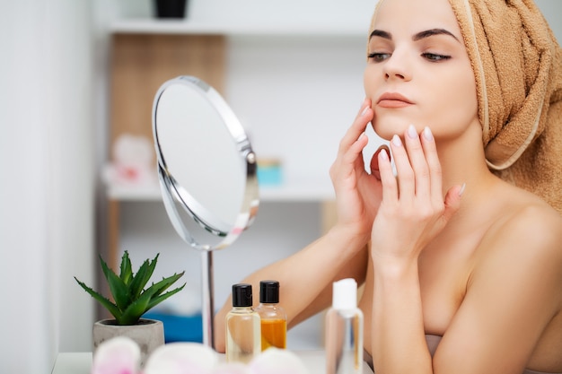 Довольно молодая женщина наносит макияж на лицо в ванной комнате