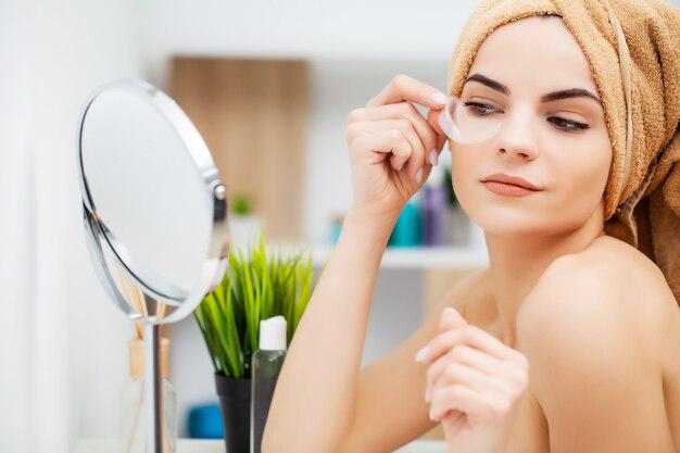 Pretty young woman puts patches under the eyes in the bathroom