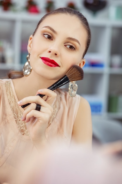 Pretty young woman putting a brush to the cheek while applying makeup on her face