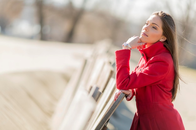 Pretty young woman in red coat by the wooden fence