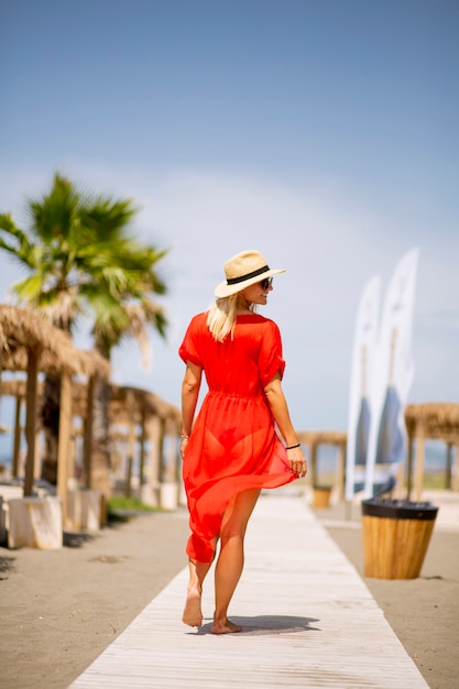 Pretty young woman in red dress walking on a beach at summer