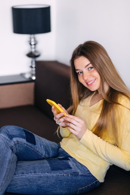 Pretty young woman relaxing at home on a sofa with her mobile ph