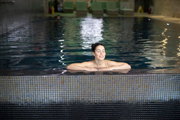 Pretty young woman relaxing on the poolside of indoor swimming pool