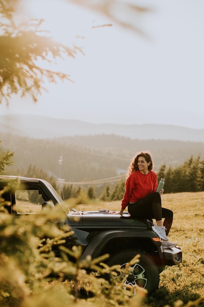 Foto bella giovane donna che si rilassa sul cofano di un veicolo fuoristrada in campagna