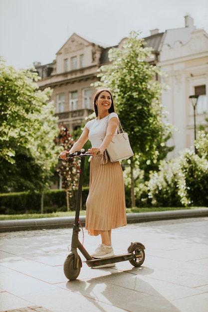 Pretty young woman riding an electric scooter on a street