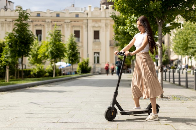 Pretty young woman riding an electric scooter on a street