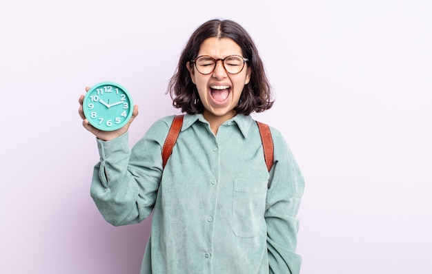 Pretty young woman shouting aggressively, looking very angry. alarm clock concept