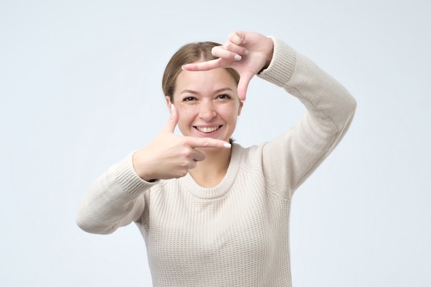 Pretty young woman showing a frame from the hands and smiling friendly