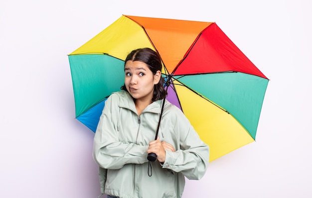 かなり若い女性が混乱し、不確かな雨と傘の概念を肩をすくめる