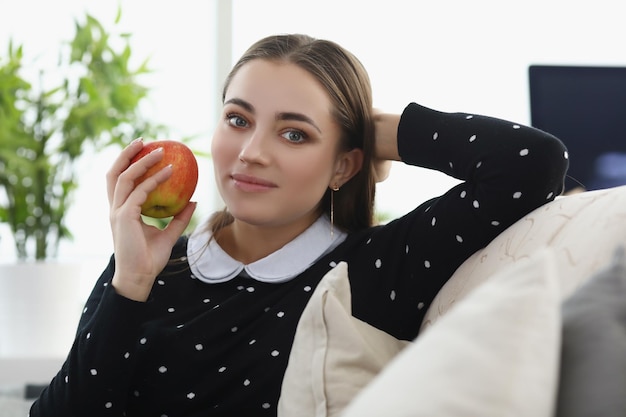 Pretty young woman sit comfy on couch at home fresh apple fruit as snack