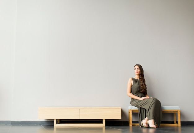 Pretty young woman sitting on bench in the modern room by gray wall