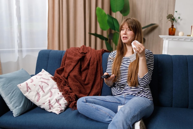 Photo pretty young woman sitting on the couch watching a melodrama and crying