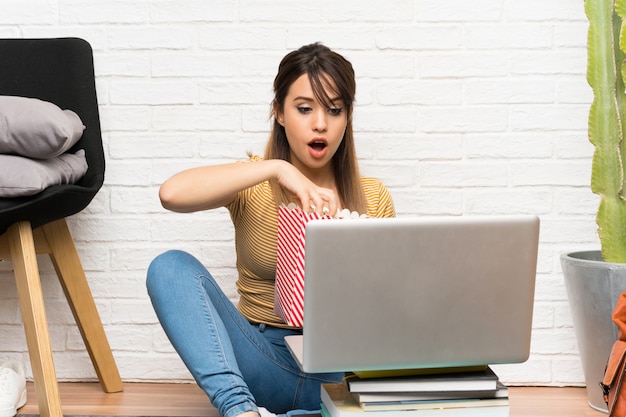 Pretty young woman sitting on the floor at indoors holding popcorns