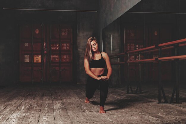 Pretty young woman slavic in sports uniform works out in evening in an old gym, doing stretching exercises in front of mirror. Concept of healthy lifestyle, sport and exercise in gym. Copy space