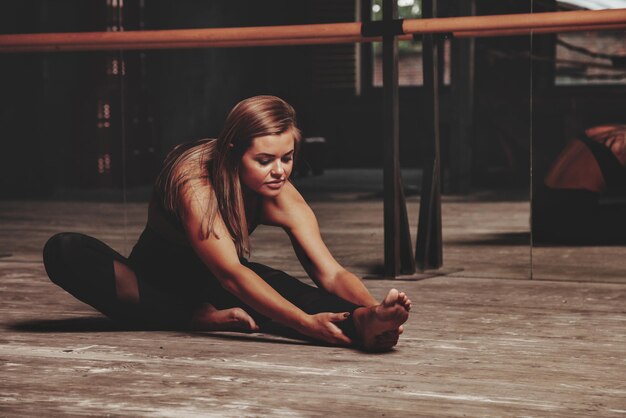 Pretty young woman slavic in sports uniform works out in evening in an old gym, doing stretching exercises in front of mirror. Concept of healthy lifestyle, sport and exercise in gym. Copy space