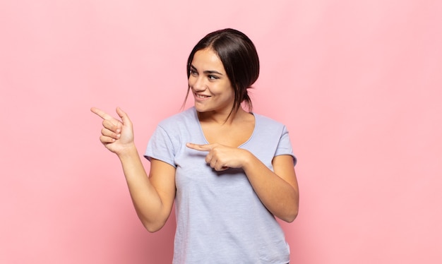 Pretty young woman smiling cheerfully and casually pointing to copy space on the side, feeling happy and satisfied