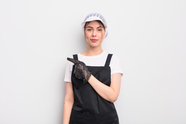 Pretty young woman smiling cheerfully feeling happy and pointing to the side fishmonger concept