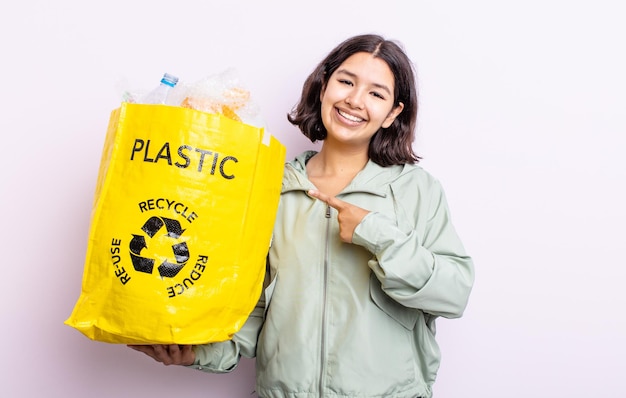 Pretty young woman smiling cheerfully, feeling happy and pointing to the side. plastic recycling concept