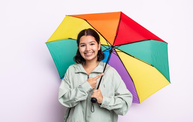 元気に笑って、幸せを感じて、横を指しているかなり若い女性。雨と傘のコンセプト