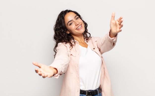 Pretty young woman smiling cheerfully giving a warm, friendly, loving welcome hug, feeling happy and adorable