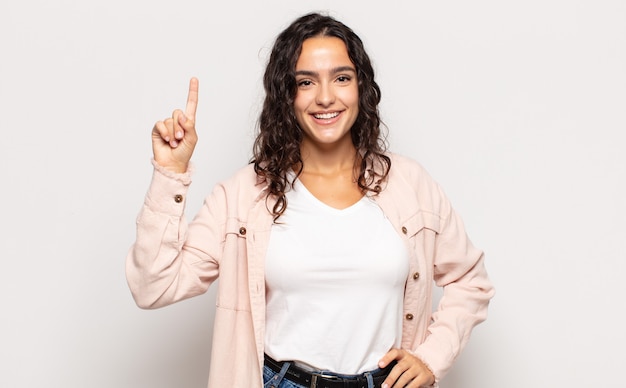 Pretty young woman smiling cheerfully and happily, pointing upwards with one hand to copy space