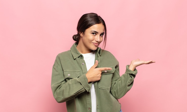 Photo pretty young woman smiling, feeling happy, carefree and satisfied, pointing to concept or idea on copy space on the side