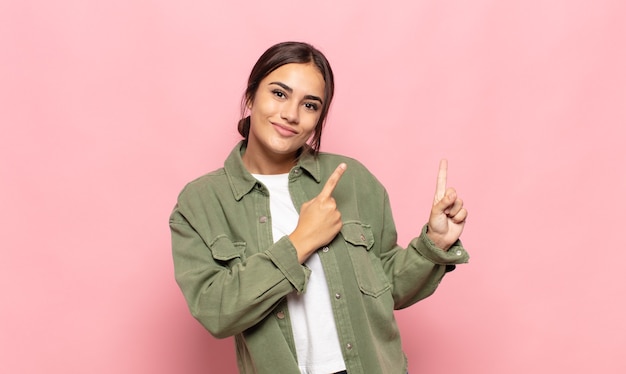 Photo pretty young woman smiling happily and pointing to side and upwards with both hands showing object