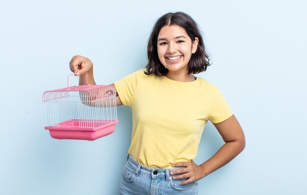 腰に手を当てて自信を持って幸せそうに笑っているかなり若い女性。ペットケージのコンセプト