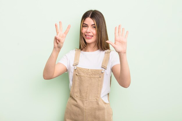 pretty young woman smiling and looking friendly, showing number eight or eighth with hand forward, counting down