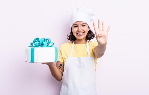 Donna abbastanza giovane che sorride e che sembra amichevole, mostrando il numero quattro. chef che cucina una torta