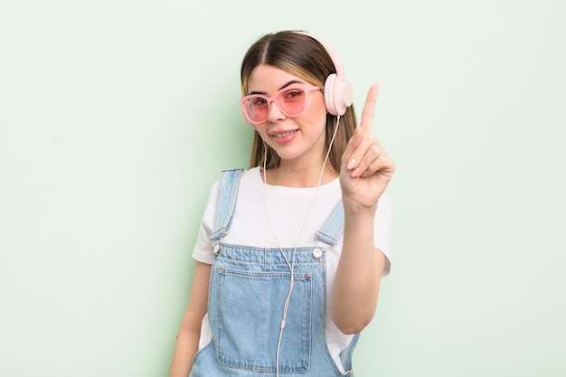 Pretty young woman smiling and looking friendly, showing number one. listening music concept