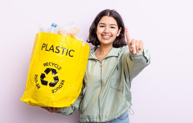 かなり若い女性が笑顔でフレンドリーに見え、ナンバーワンを示しています。プラスチックリサイクルの概念