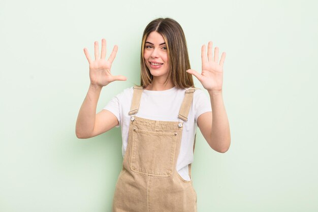 pretty young woman smiling and looking friendly, showing number ten or tenth with hand forward, counting down