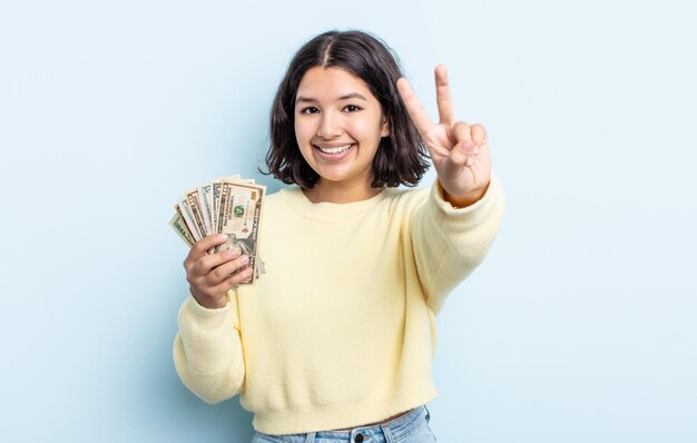 Pretty young woman smiling and looking friendly showing number two dollar banknotes concept