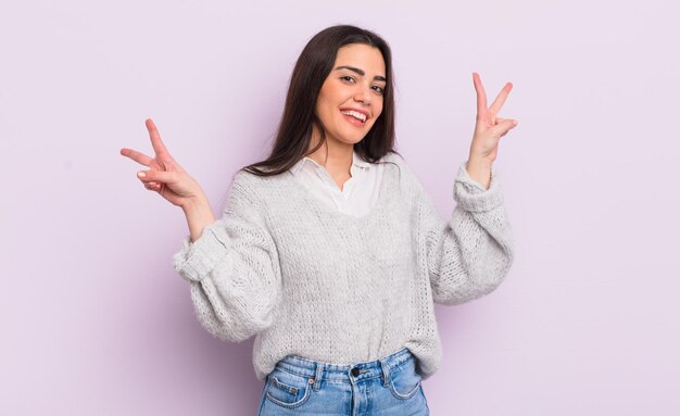 Pretty young woman smiling and looking happy, friendly and satisfied, gesturing victory or peace with both hands