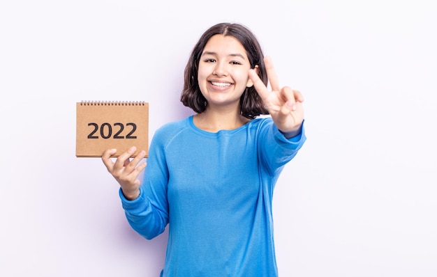 Pretty young woman smiling and looking happy, gesturing victory or peace. 2022 calendar concept