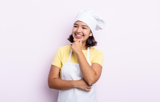 Pretty young woman smiling with a happy confident expression with hand on chin chef concept