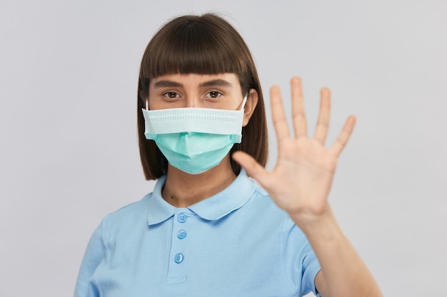 Pretty young woman in sterile disposal protection mask on face showing to keep distance with her arm