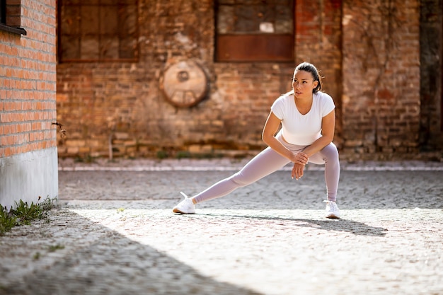 Pretty young woman stretching during training in the urban environment