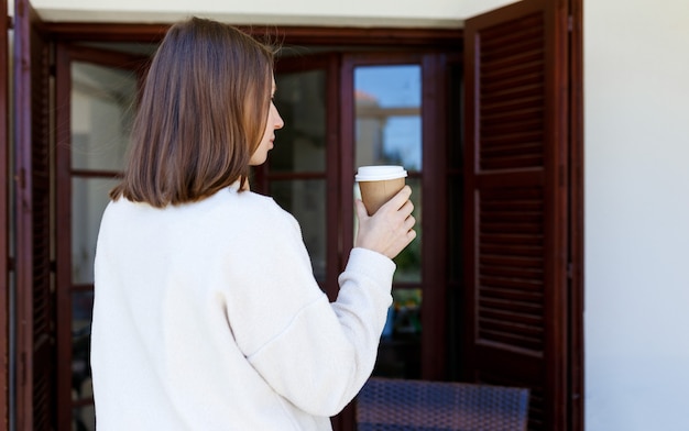 Pretty young woman in stylish grey sweater holding cup in hands warm soft cozy image details drinkin