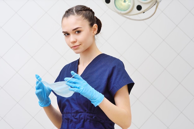 Pretty young woman in a surgical suit puts on a sterile mask