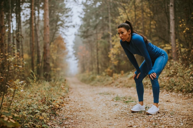 Pretty young woman take a break during outdoor exercise on the forest trail at autumn