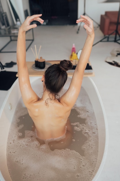 Pretty young woman taking bath at home back view