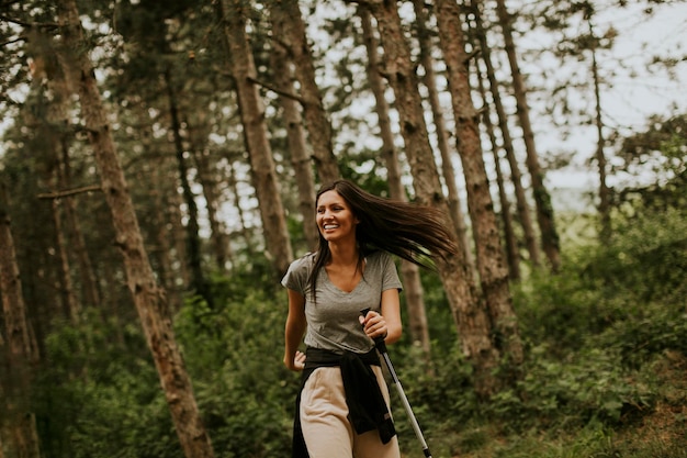 Красивая молодая женщина гуляет с трекинговыми палками в лесу с рюкзаком