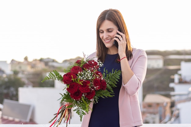 Pretty young woman talking on her phone with bouquet of red roses