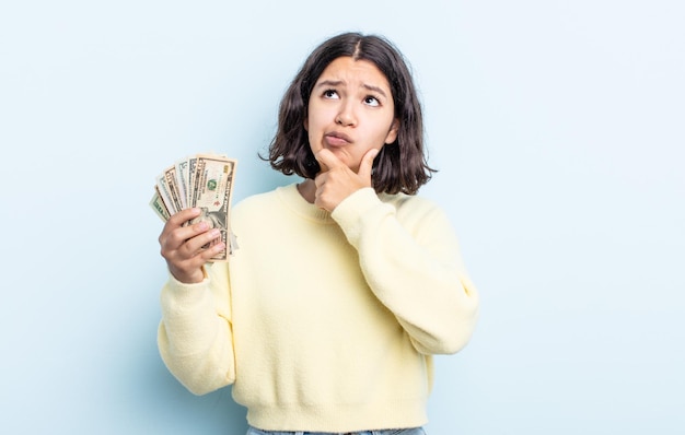 Pretty young woman thinking, feeling doubtful and confused. dollar banknotes concept