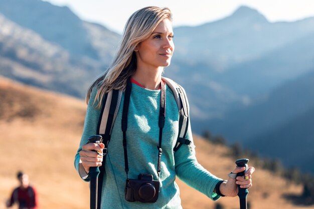 Pretty young woman traveler with backpack looking to the side while walking on mountain.