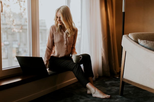 Pretty young woman using laptop and sitting by window