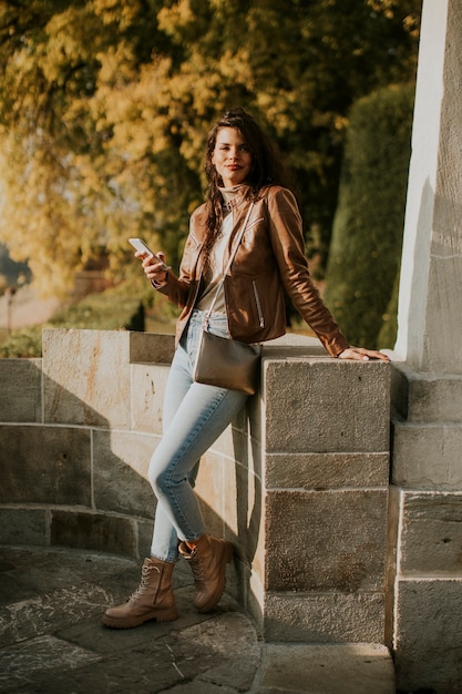 Pretty young woman using mobile phone while standing in the autumn park